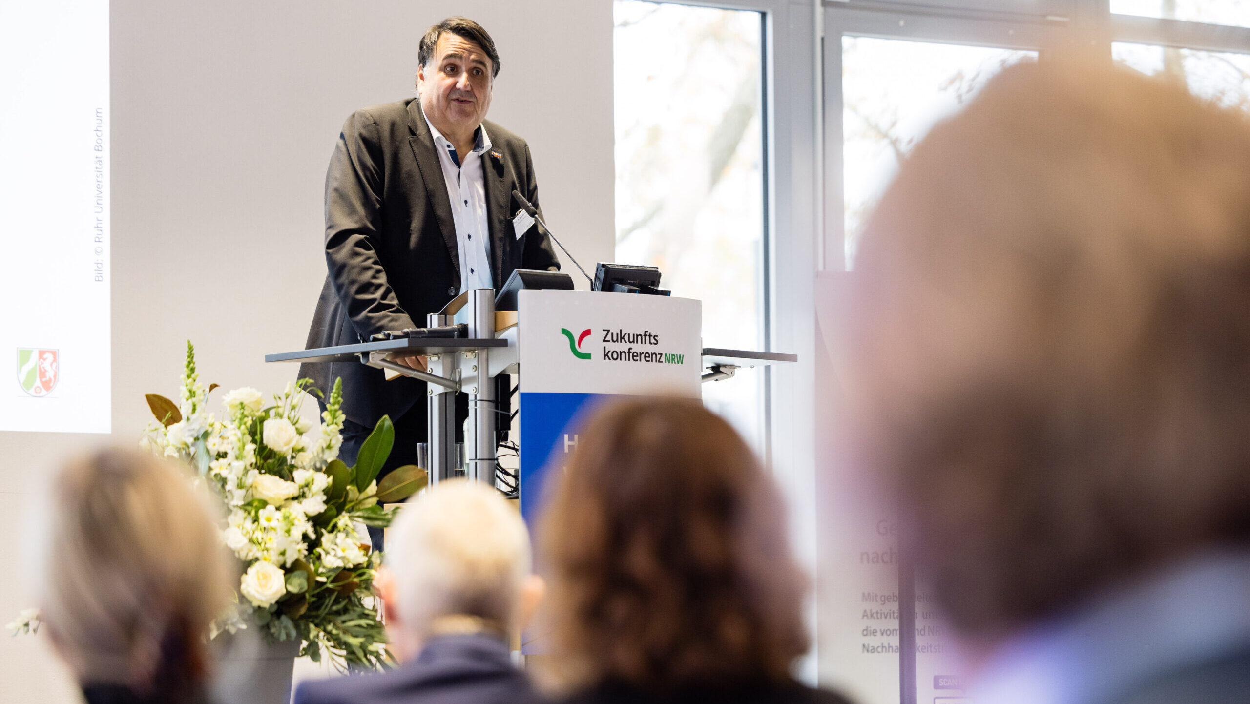 Redner steht auf der Bühne und hält Vortrag.