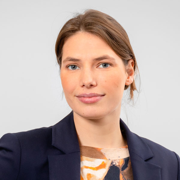 Ein Porträt einer Frau mit braunen Haaren, die sie zu einem Zopf nach hinten gebunden hat. Sie trägt ein dunkelblaues Sakko und blickt freundlich in die Kamera.