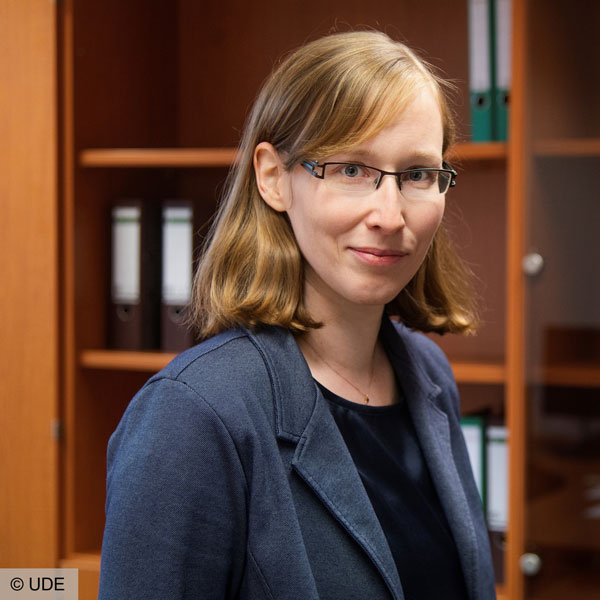 Porträtbild einer Frau mit schulterlangen, hellbraunen Haaren und blauen Augen. Sie trägt eine eckige Brille, eine schwarze Bluse und einen dunkelgrauen Blazer. Sie lächelt freundlich in die Kamera.