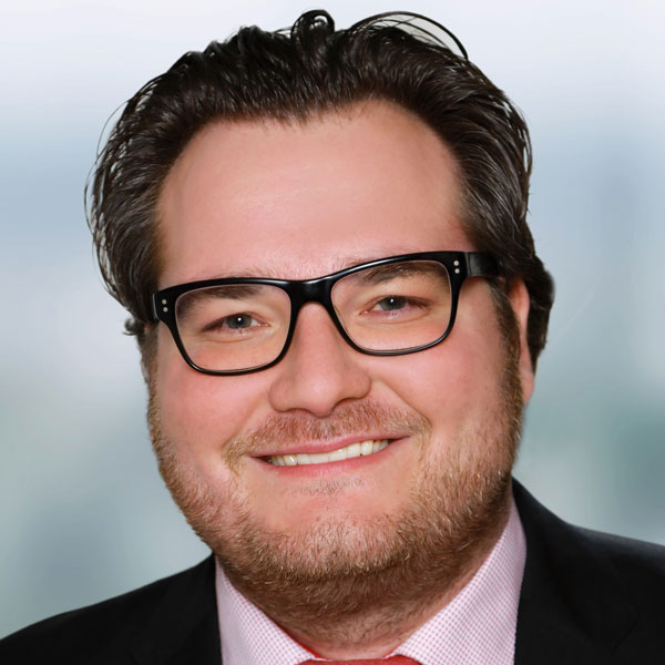 Prof. Dr. Marco Jung Ein Porträtbild eines Mannes mit dunkelbraunen Haaren. Er trägt eine rechteckige, dunkle Brille und einen Anzug und lächelt in die Kamera.