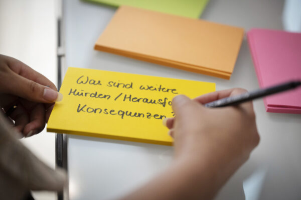 Mensch schreibt etwas auf Post-it.